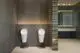 Weißer Sensor-WC-Armatur von Ideal Standard, batteriebetrieben, vor einer modernen Wandgestaltung mit grauen Fliesen und geschmackvollem Licht.